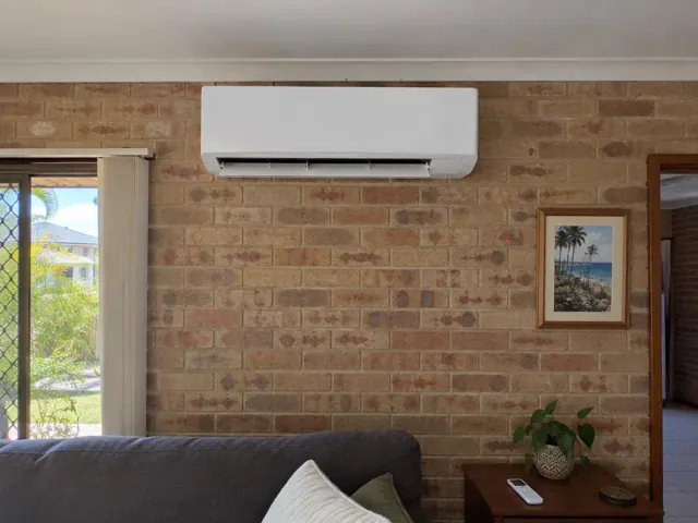 Running split system mounted high on a brick interior wall above a lounge room in Coombabah