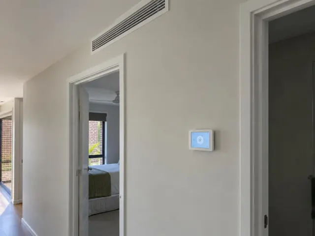 Hallway with a ceiling air grille and wall controller beside open doorways in a modern home in Southport