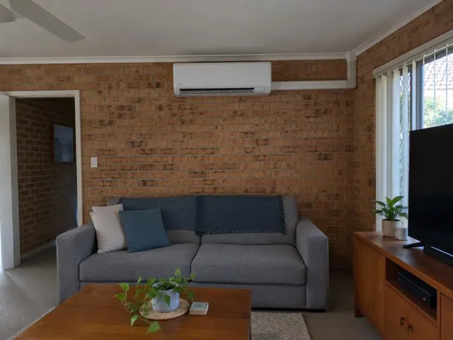 Wall-mounted split system above a grey sofa on an exposed brick wall in a living room in Labrador